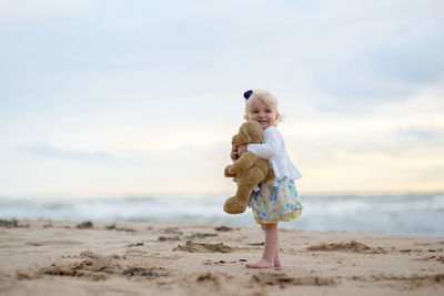 Happy girl holding teddy bear while standing at beach