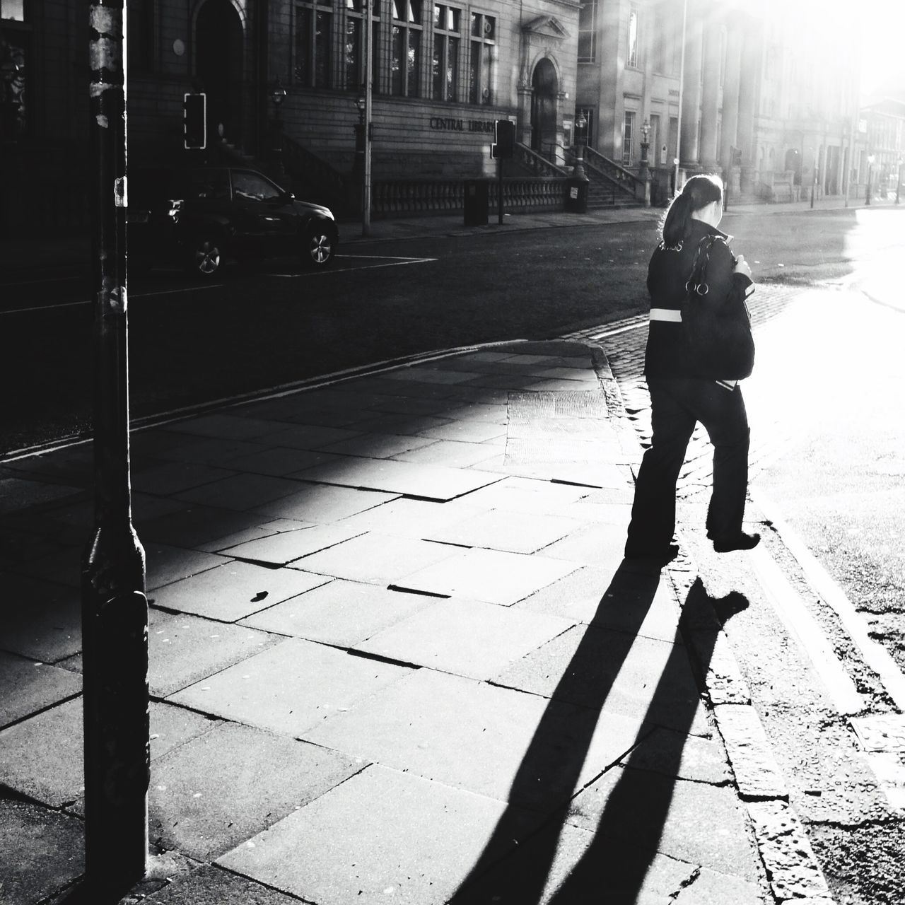 full length, lifestyles, building exterior, street, leisure activity, city, sidewalk, built structure, architecture, standing, water, casual clothing, rear view, city life, walking, sunlight, outdoors, shadow