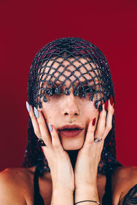 Portrait of young woman wearing net scarf against red background