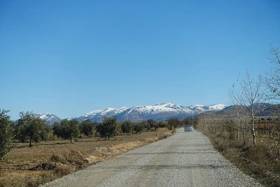 Road amidst agricultural field against clear blue sky