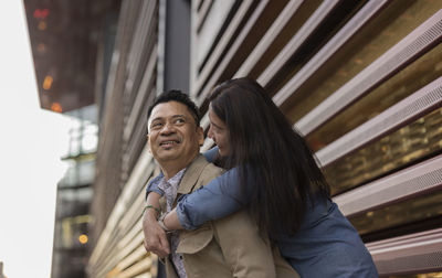 Happy woman embracing man from behind in front of building