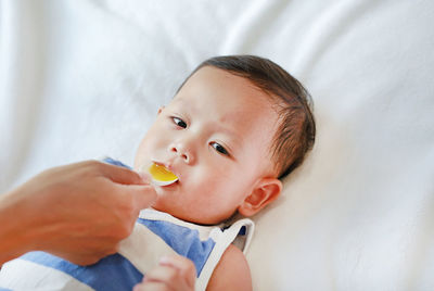 Cropped hand of mother feeding medicine to baby boy lying on bed at home