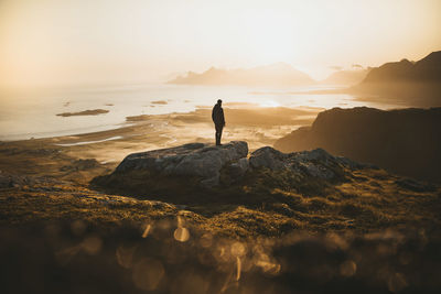 Man standing on rocks at shore against sky during sunset