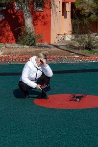 Full length of woman crouching while holding remote control