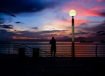 Silhouette man standing by railing against sky during sunset