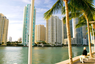 Man sitting by lake on bench in city