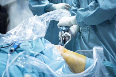 Midsection of surgeons operating knee in hospital