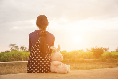 Rear view of woman sitting toy against sky during sunset
