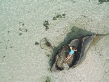 Drone shot of woman relaxing on rock at beach