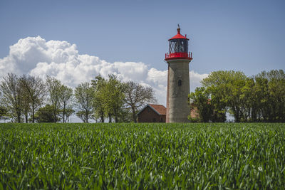 Lighthouse by trees on field against sky