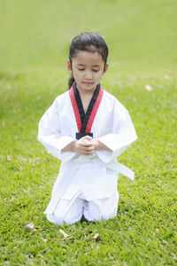 Girl with hands clasped wearing karate uniform while meditating on grassy field at park
