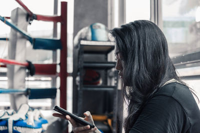 Side view of young woman using mobile phone while sitting in gym