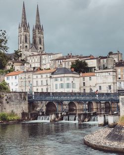 Arch bridge over river by buildings against sky