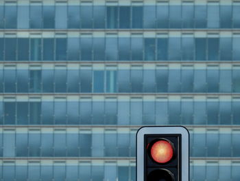 Red traffic light against blue glass building