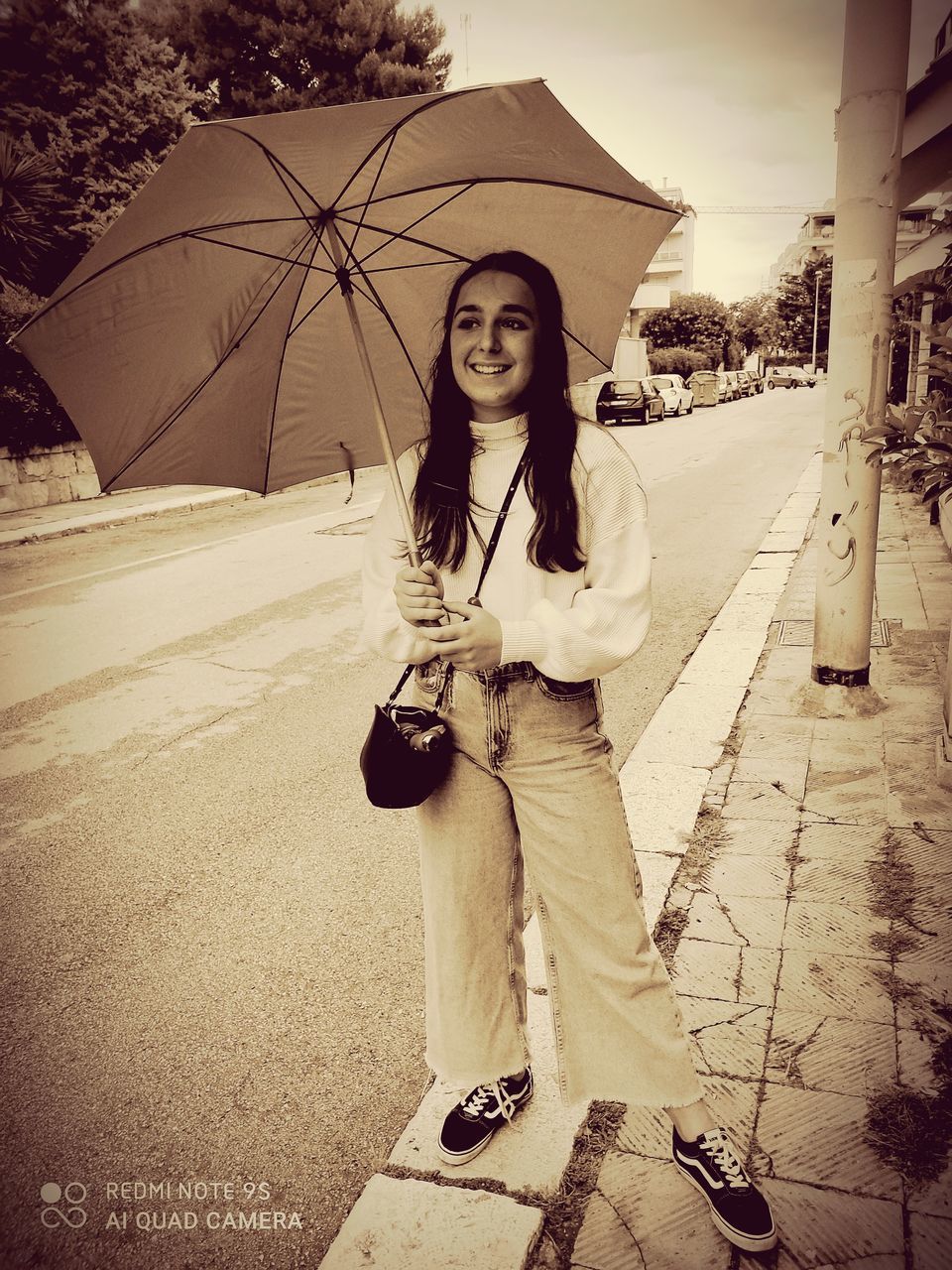 FULL LENGTH PORTRAIT OF SMILING WOMAN STANDING ON RAINY DAY IN CITY