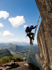 Side view of hiker climbing on mountain against sky