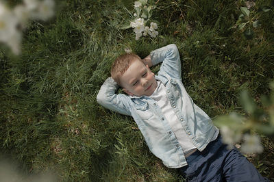 Cute preschooler boy in denim shirt folded his arms under his head and rests on fresh green grass 