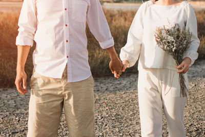 Midsection of wedding couple walking on field