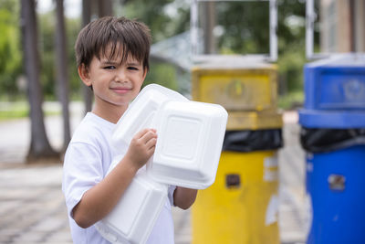 Portrait of smiling boy holding camera while standing outdoors