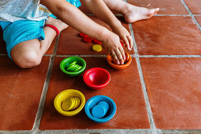 Low section of boy playing with multi colored coins and containers on flooring