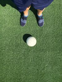 Low section of person standing by golf ball on sunny day