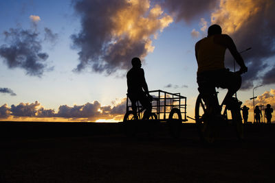 Rear view of silhouette man riding bicycle against sky during sunset