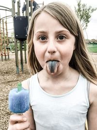 Portrait of cute girl with popsicle sticking out tongue on field