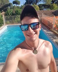 Portrait of shirtless smiling young man against swimming pool during summer