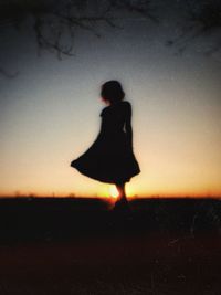 Silhouette woman walking on field during sunset