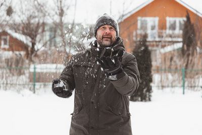 A man throws snowballs in the yard of a private house on a frosty day, snow games in the air.