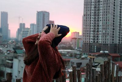 Side view of teenage girl with head in hands standing against buildings during sunset