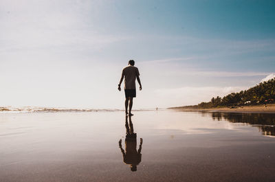 Rear view of man standing at beach against sky