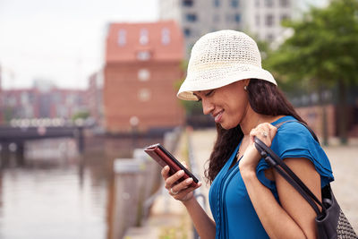 Side view of smiling mid adult woman using mobile phone by river