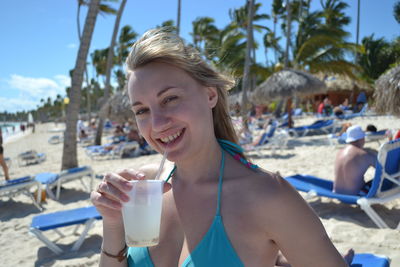 Portrait of smiling young woman drinking water from beach
