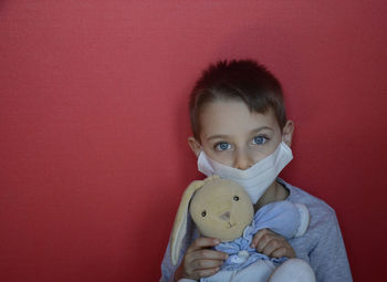 Portrait of cute boy holding toy against red wall