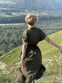 A young woman in a long dress fluttering in the wind stands on a mountainside in altai, russia. 