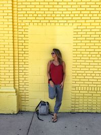 Full length of woman leaning on yellow brick wall