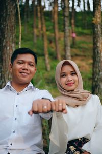 Portrait of smiling couple showing wedding rings while standing against trees in forest