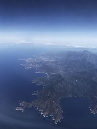 Aerial view of sea and mountains against blue sky