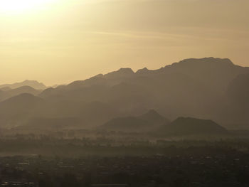 Scenic view of silhouette mountain range against sky at dawn during foggy weather