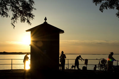 Silhouette people by sea against sky during sunset