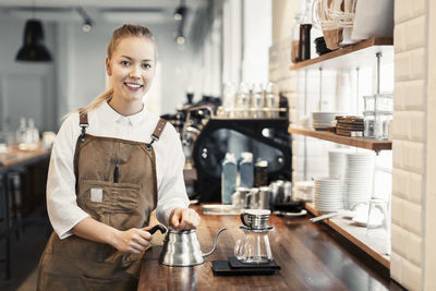 Portrait of happy female barista standing at counter in coffee shop