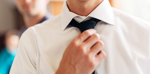 Midsection of bridegroom wearing white shirt adjusting necktie