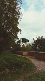 Footpath by trees against cloudy sky