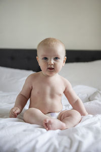 Cute baby boy sitting on bed at home