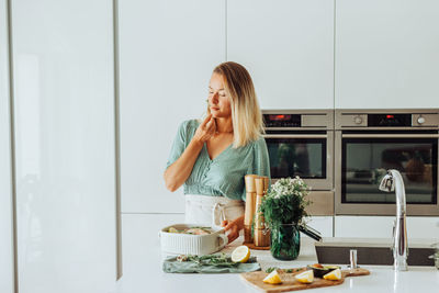 Woman smelling aromatic herbs while standing at domestic kitchen
