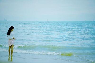 Rear view of woman standing at beach against sky