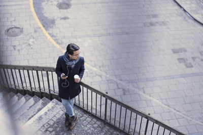 Handsome man with smartphone and paper cup standing on steps