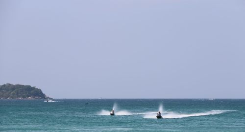 People riding motorboats on sea against clear blue sky