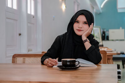 Portrait of young woman using mobile phone at table